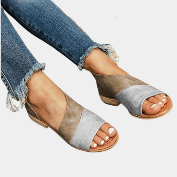 Vrouw draagt modieuze bruine en grijze sandalen met open teen, gecombineerd met gescheurde jeans. Trendy zomerschoenen voor dames.