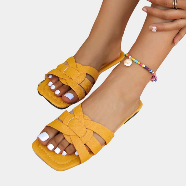 Gele dames sandalen met gevlochten bandjes, gedragen met een kleurrijke enkelband. Perfect voor zomerse outfits en strandmode.