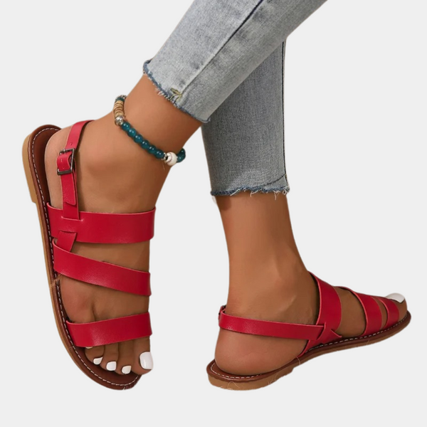 Rode leren sandalen met gespsluiting, gedragen met blauwe jeans en enkelarmband. Stijlvolle zomerschoenen voor dames.