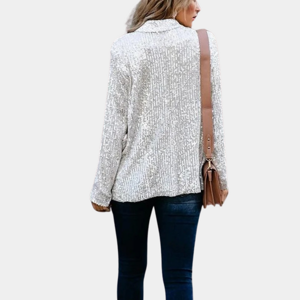 Vrouw in zilveren paillettenblouse met lange mouwen, draagt een bruine schoudertas en donkere jeans, modieuze outfit, achteraanzicht.