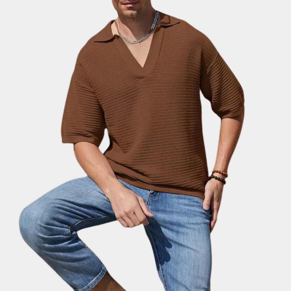 Man in bruine geribbelde trui met korte mouwen en blauwe jeans, poseert tegen witte achtergrond. Modieuze herenkleding, casual stijl.