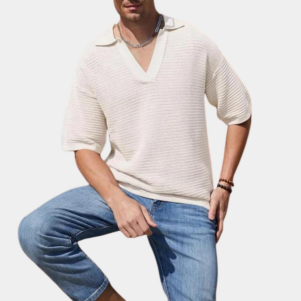 Man in witte gebreide trui met V-hals en korte mouwen, gecombineerd met blauwe jeans. Casual herenkleding, modetrend, zomeroutfit.