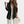 Vrouw in zwarte geribbelde blazer, witte kanten top en crèmekleurige broek, houdt een crèmekleurige clutch vast. Modieuze dameskleding, herfststijl.