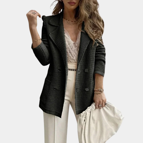 Vrouw in zwarte geribbelde blazer, witte kanten top en crèmekleurige broek, houdt een crèmekleurige clutch vast. Modieuze dameskleding, herfststijl.