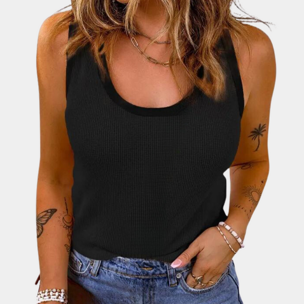 Vrouw in zwarte tanktop met ronde hals, blauwe jeans en sieraden. Trendy zomeroutfit, casual mode, tatoeages op armen.