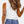 Vrouw in witte tanktop en blauwe jeans, met golvend haar en armbanden, toont rug en tatoeage van oog op arm. Casual mode, zomeroutfit.