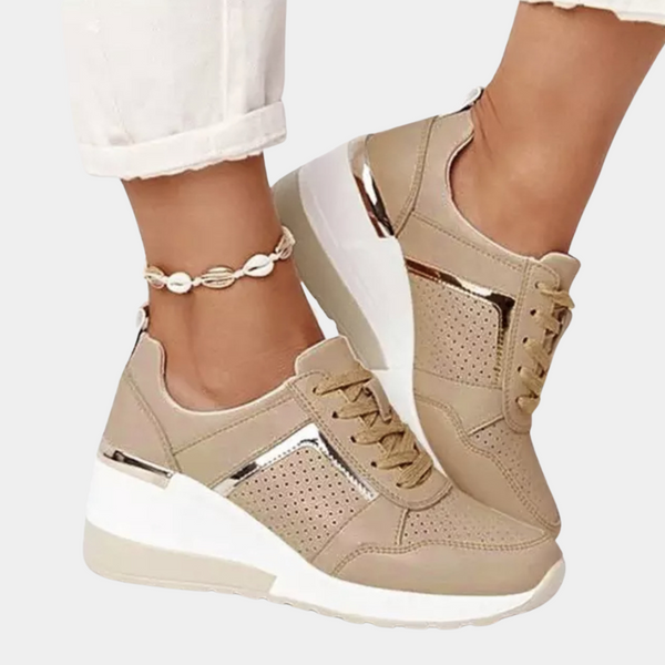 Beige sneakers met sleehak, metallic details en perforaties, gedragen met witte broek. Modieuze damesschoenen, comfortabel en stijlvol.