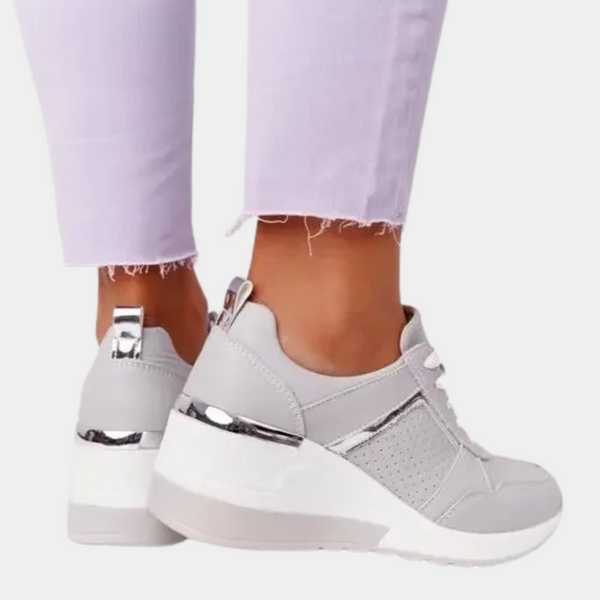 Witte dames sneakers met sleehak, zilveren details en perforaties, gedragen met lichtpaarse broek. Modieuze en comfortabele schoenen.