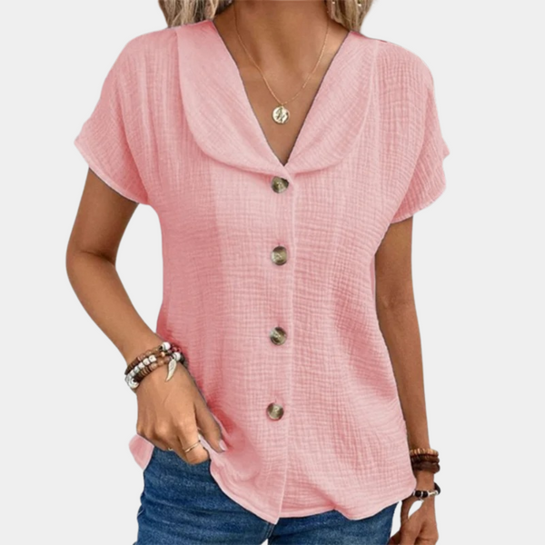 Vrouw draagt roze blouse met knoopsluiting en korte mouwen, gecombineerd met blauwe jeans. Modieuze dameskleding, casual zomeroutfit.