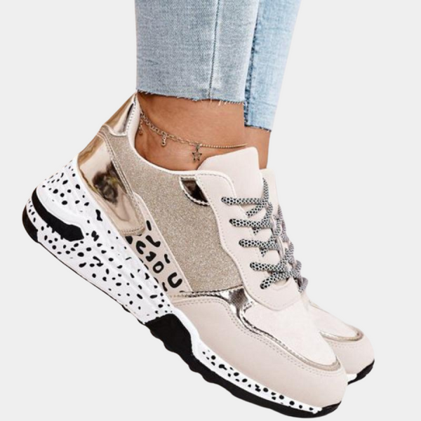 Dames sneakers in goud en beige met glinsterende details, zwarte en witte zool, en veters. Modieuze sportschoenen voor casual en sportieve outfits.