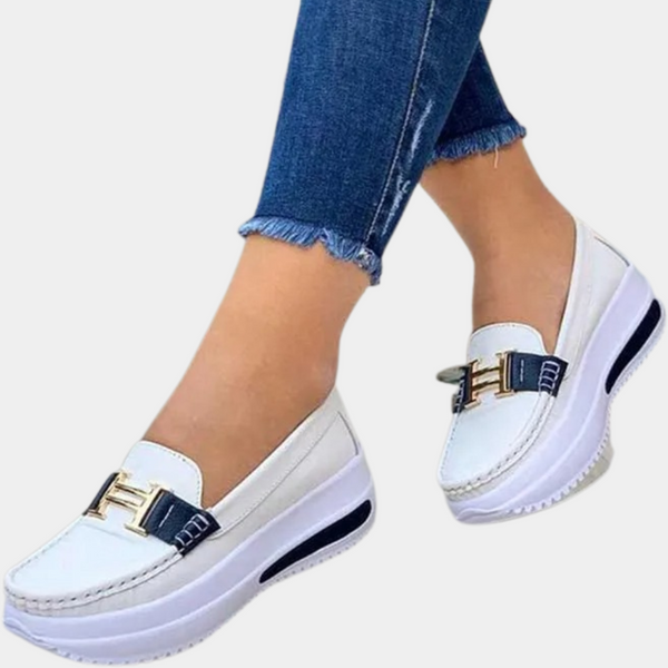 Witte dames loafers met verhoogde zool, gouden gesp en blauwe accenten, gedragen met jeans. Comfortabele en stijlvolle schoenen voor dagelijks gebruik.