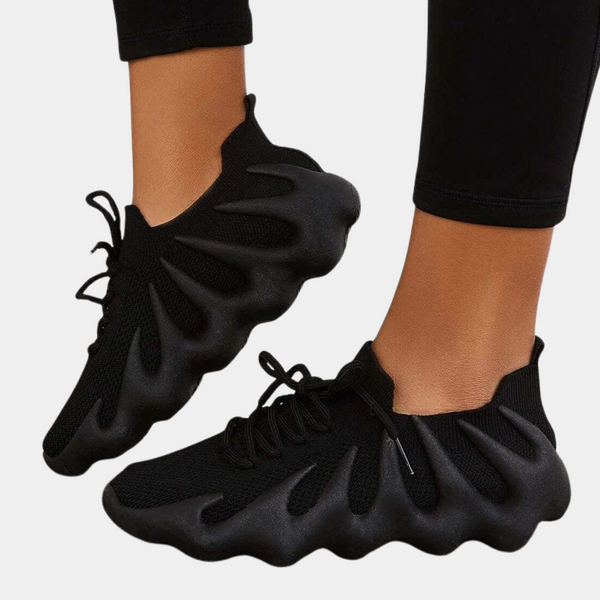 Zwarte futuristische sneakers met golvende zool, gedragen door persoon. Moderne sportschoenen, ademend materiaal, trendy design, comfortabele pasvorm.