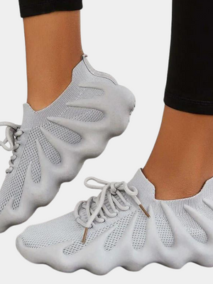 Grijze sneakers met golvende zool en veters, gedragen door persoon in zwarte legging. Moderne, comfortabele sportschoenen voor dagelijks gebruik.