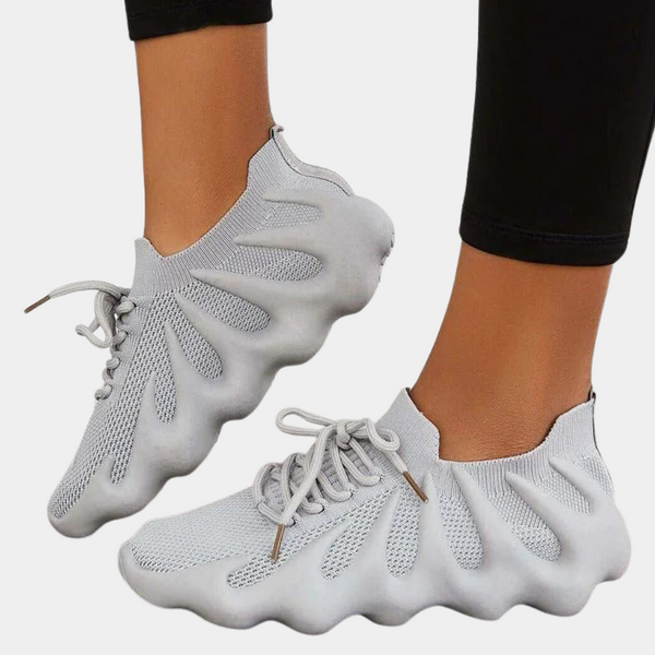 Grijze sneakers met golvende zool en veters, gedragen door persoon in zwarte legging. Moderne, comfortabele sportschoenen voor dagelijks gebruik.