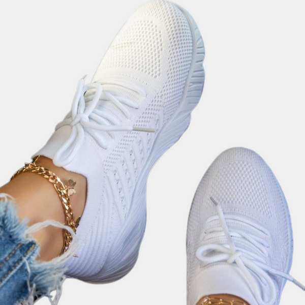 Witte sneakers met gebreid bovenwerk en dikke zool, gedragen met gouden enkelbandjes en gescheurde jeans. Trendy damesmode, comfortabele sportschoenen.