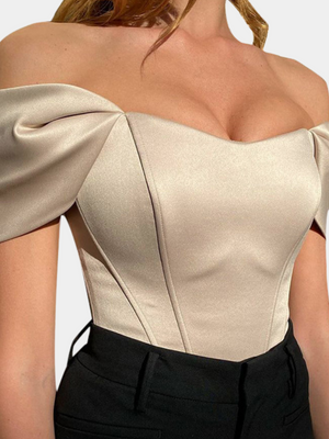 Vrouw in elegante off-shoulder top, abrikooskleurig, met pofmouwen en getailleerd ontwerp. Perfect voor avondkleding en modieuze gelegenheden.