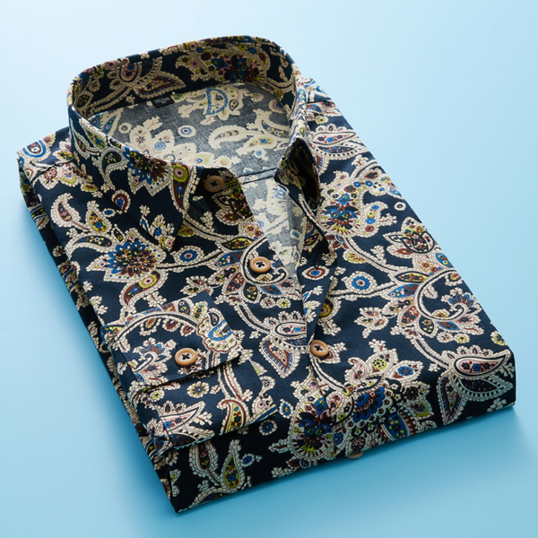 Opgevouwen herenoverhemd met paisleyprint in marineblauw, kleurrijke details en houten knopen, op een lichtblauwe achtergrond.