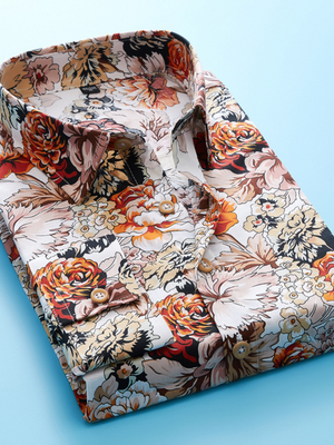 Opgevouwen herenoverhemd met kleurrijke bloemenprint, oranje en beige tinten, op een lichtblauwe achtergrond. Perfect voor modieuze casual outfits.
