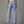 Vrouw in lichtblauwe denim jeans met wijde pijpen, hoge taille en zakken, tegen een grijze achtergrond. Trendy damesmode, casual stijl.