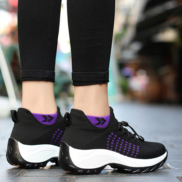 Zwarte en paarse sportschoenen met dikke witte zolen, gedragen door persoon in zwarte broek. Comfortabele sneakers voor dames, ideaal voor hardlopen.