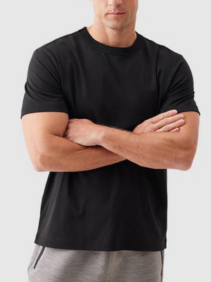 Zwarte heren T-shirt, korte mouwen, ronde hals, casual stijl, gedragen door man met gekruiste armen, grijze achtergrond.