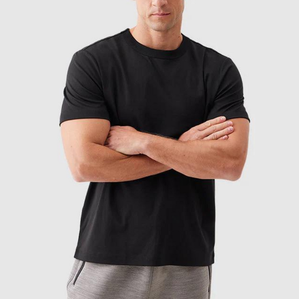 Zwarte heren T-shirt, korte mouwen, ronde hals, casual stijl, gedragen door man met gekruiste armen, grijze achtergrond.