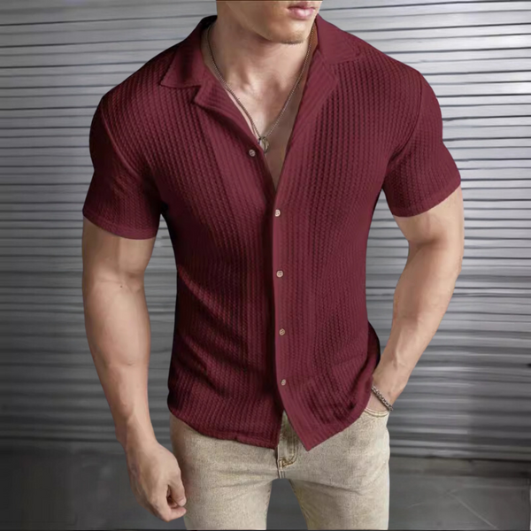 Man in wijnrode gebreide polo met korte mouwen, open kraag en beige broek, voor metalen achtergrond. Stijlvolle herenkleding, casual mode.