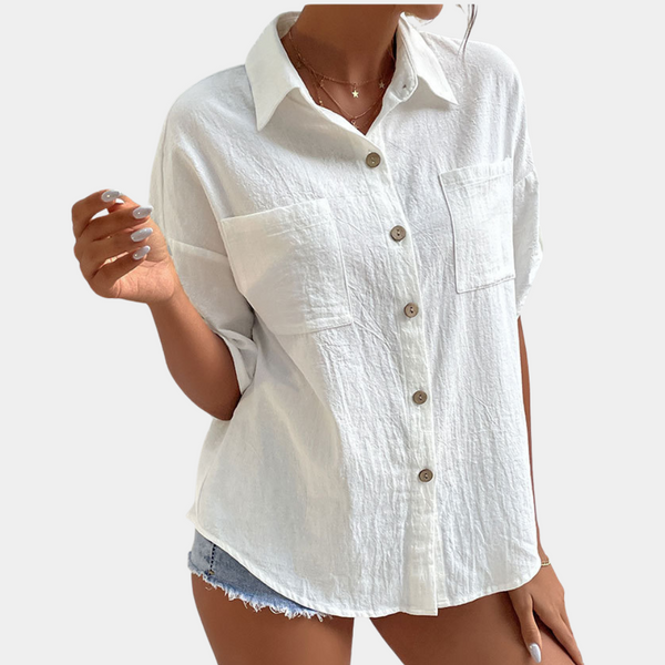 Witte damesblouse met korte mouwen, knoopsluiting en borstzakken, gedragen met denim shorts. Perfect voor casual zomeroutfits.