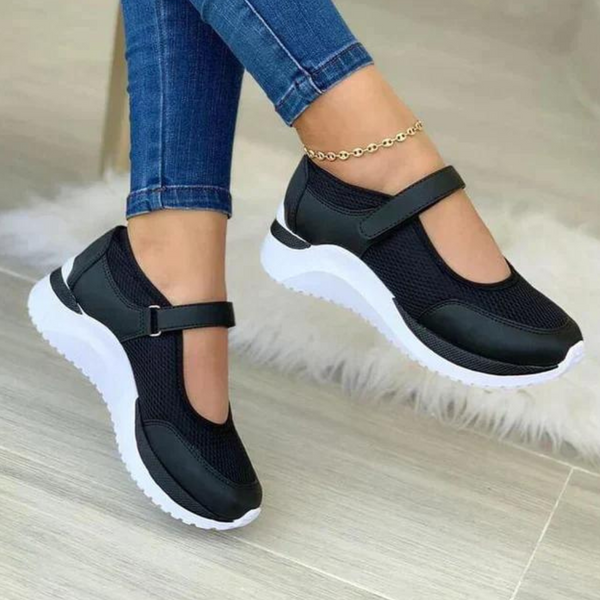 Zwarte dames sneakers met klittenbandsluiting en witte zool, gedragen met blauwe jeans. Comfortabele en modieuze schoenen voor dagelijks gebruik.