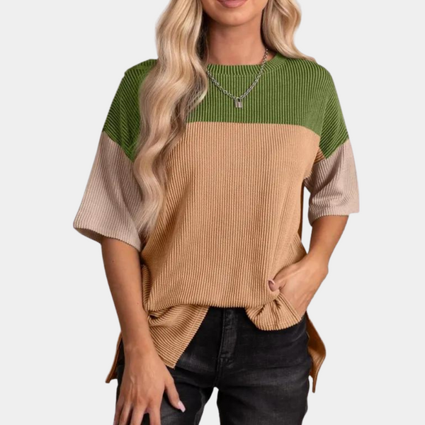 Vrouw in modieuze, geribbelde trui met groene, beige en bruine kleurblokken, gecombineerd met zwarte jeans. Trendy dameskleding, casual stijl.