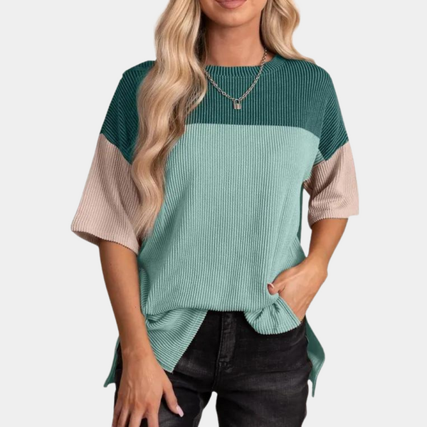Vrouw draagt lichtblauwe geribbelde trui met korte mouwen en kleurblokken, gecombineerd met zwarte jeans. Modieuze dameskleding, casual stijl.