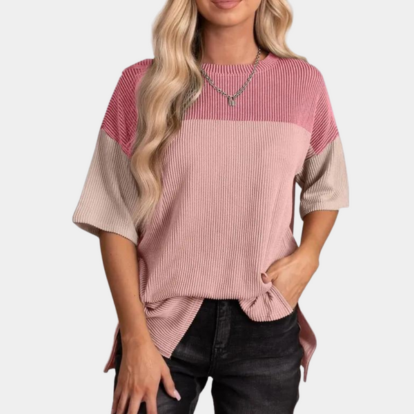 Vrouw draagt roze en beige geribbelde trui met korte mouwen, gecombineerd met zwarte jeans. Modieuze dameskleding, casual stijl.
