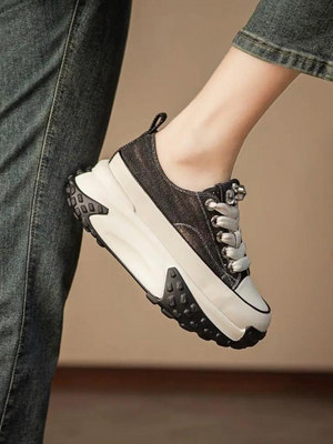 Zwarte platform sneaker met dikke zool, witte accenten en veters, gedragen door persoon in spijkerbroek. Trendy damesschoen, casual stijl.
