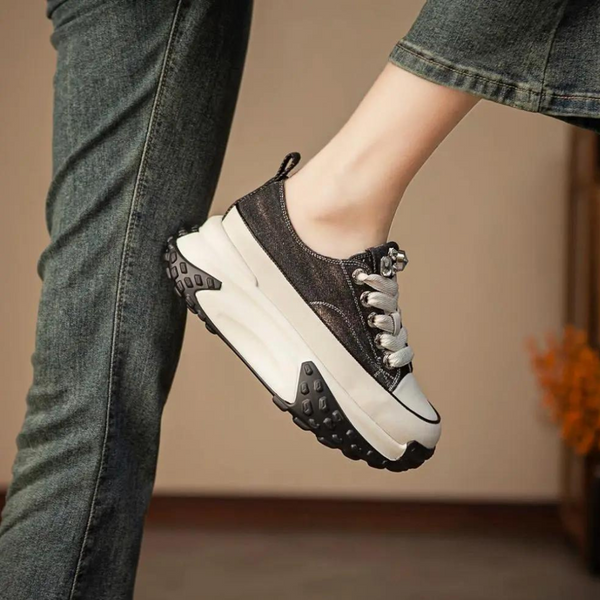 Zwarte platform sneaker met dikke zool, witte accenten en veters, gedragen door persoon in spijkerbroek. Trendy damesschoen, casual stijl.