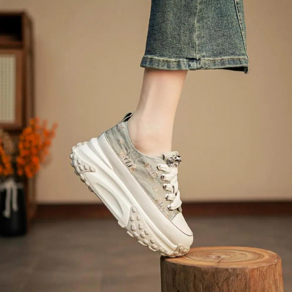 Grijze platform sneaker met dikke zool, witte veters en denim afwerking, gedragen door persoon in spijkerbroek. Trendy damesmode, casual stijl.