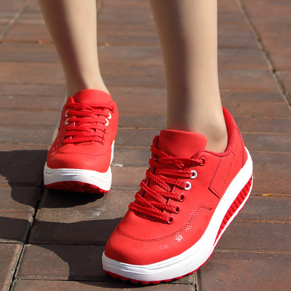 Rode damessneakers met dikke zool, vetersluiting en witte accenten, gedragen op een bakstenen trottoir. Comfortabele en modieuze sportschoenen.
