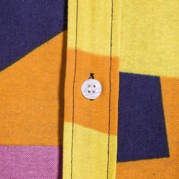 Close-up van kleurrijk geometrisch patroon op katoenen overhemd met knoop. Abstracte vormen in geel, oranje, paars en blauw. Modieuze herenkleding.