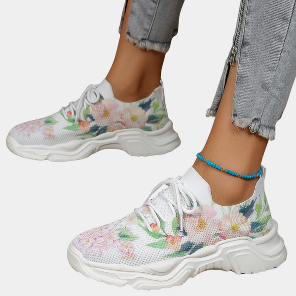 Witte damessneakers met bloemenprint, dikke zool en turquoise enkelbandje, gedragen met grijze jeans. Trendy en comfortabele schoenen.