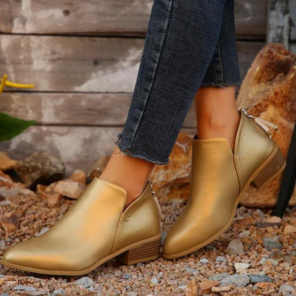 Gouden enkellaarsjes met blokhak, gedragen op grindpad. Stijlvolle damesmode, perfect voor casual en chique outfits. Comfortabele en trendy schoenen.