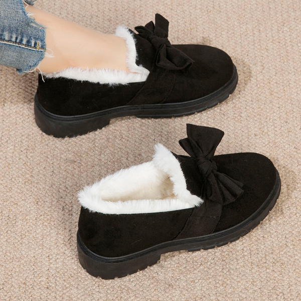 Zwarte damespantoffels met witte voering en strikdetail, comfortabele winterse huisschoenen op beige tapijt. Warme pantoffels voor binnen.