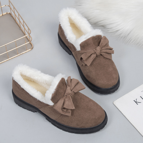 Bruine suède damesschoenen met witte bontvoering en strik, op grijze achtergrond. Warme wintermode, comfortabele schoenen, stijlvolle damesloafers.