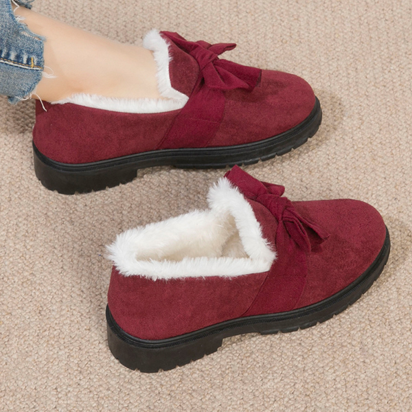 Rode suède damesschoenen met bontvoering en strik, comfortabele wintermode, warme platte schoenen op beige tapijt, casual stijl.