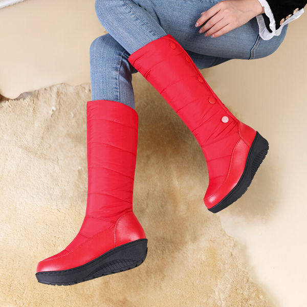 Rode dameslaarzen met knopen, gedragen met blauwe jeans op een beige tapijt. Modieuze winterlaarzen, comfortabele pasvorm, trendy design.