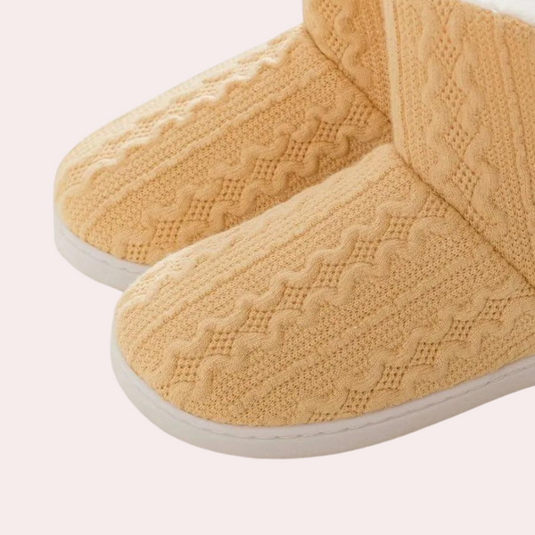Beige gebreide pantoffels met kabelpatroon, warme voering en witte zolen. Comfortabele huisschoenen voor dames, ideaal voor koude dagen.