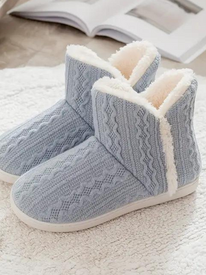 Lichtblauwe gebreide pantoffels met witte voering, warme winter sloffen voor dames, comfortabele huisschoenen op een witte vloermat.