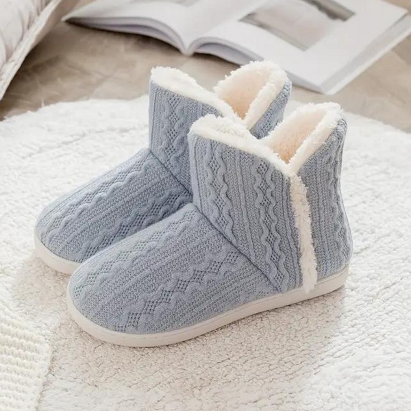 Lichtblauwe gebreide pantoffels met witte voering, warme winter sloffen voor dames, comfortabele huisschoenen op een witte vloermat.
