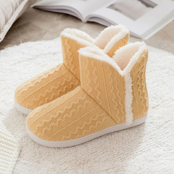 Gele gebreide pantoffels met witte voering op een zachte, witte ondergrond. Perfect voor wintercomfort en warme voeten. Gezellige huisschoenen.