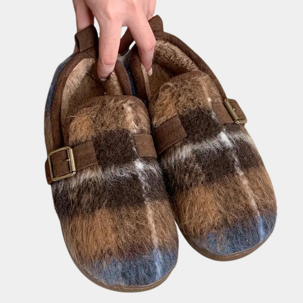 Hand houdt bruine en blauwe bontsloffen vast met gesp, warme voering. Perfect voor winter, comfortabele huispantoffels. Unisex design, trendy en stijlvol.