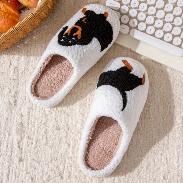 Witte pluche pantoffels met schattige berenprint, liggend op een beige tapijt naast een toetsenbord en mand. Comfortabele winterse huisschoenen.