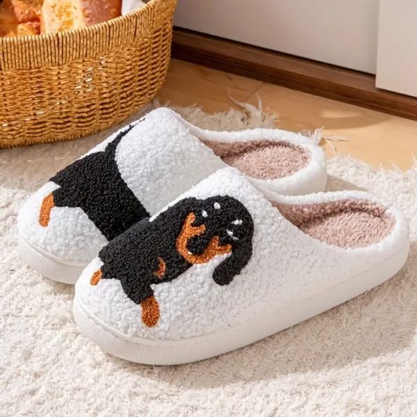 Witte pantoffels met teckelmotief, pluche voering, comfortabele dameshuisschoenen, perfect voor binnengebruik, naast een rieten mand.